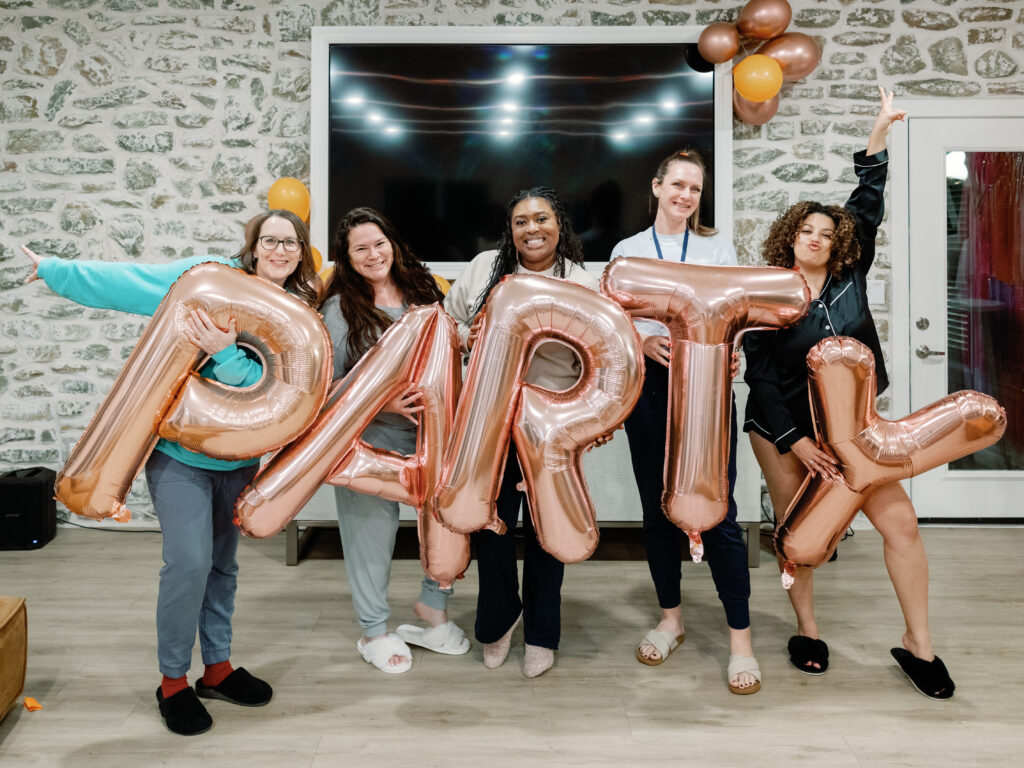 women holding balloon letters spelling party at conquer live photography retreat